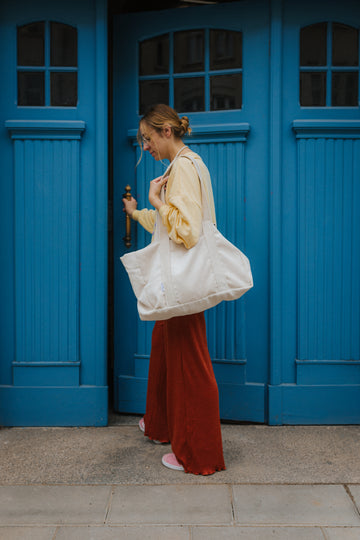 kobieta z dużą torbą sztruksową na ramię na tle niebieskich starych drzwi  