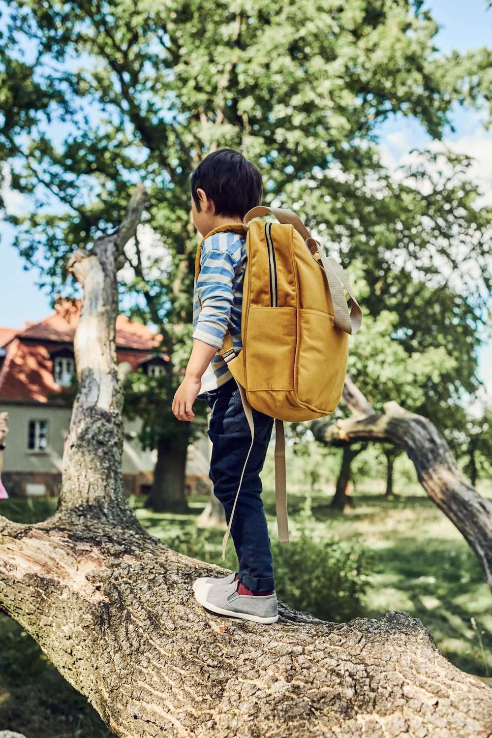 chłopiec w parku stoi na gałęzi mając Duży plecak welurowy od Bettys Home, plecak do szkoły dla chłopca plecak dla dziecka