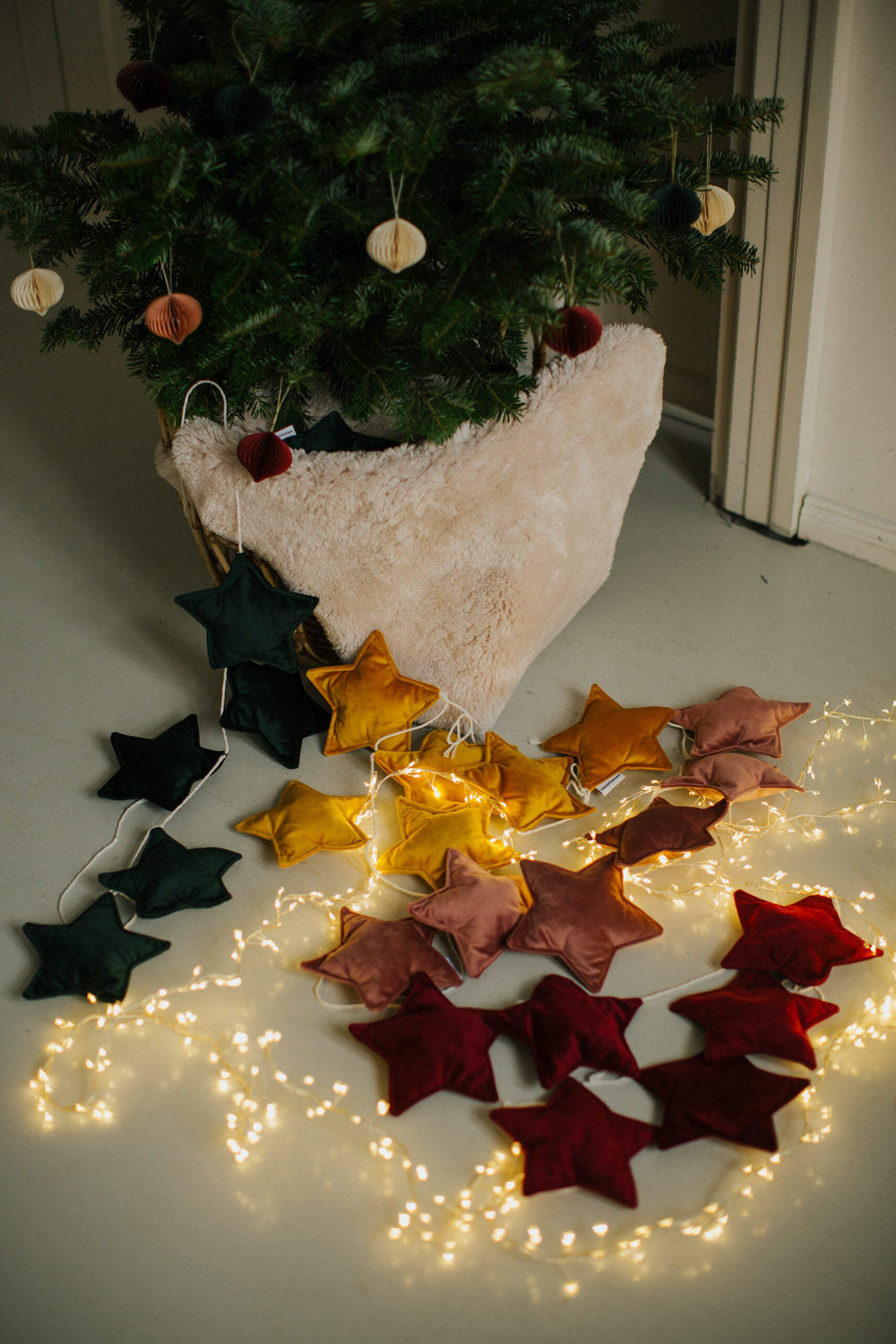 Girlandy z gwiazdek welurowych leżące na ziemi pod choinką w otoczeniu lampek świątecznych 