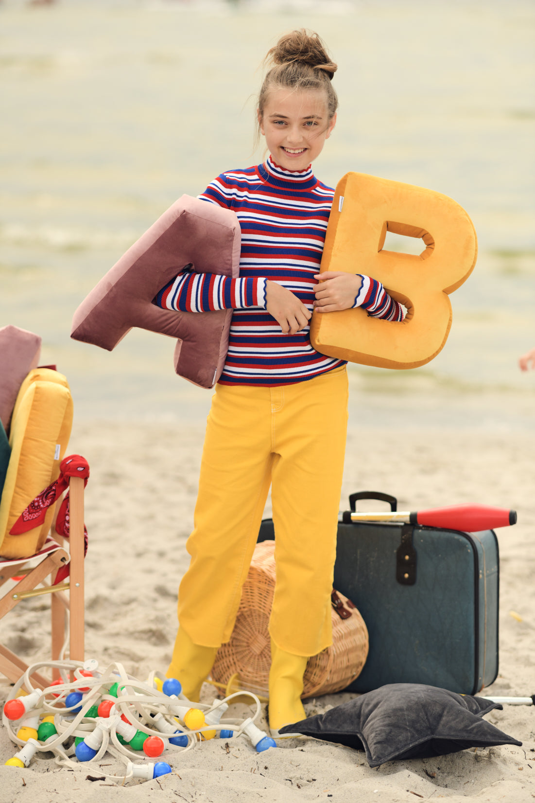 dziewczyna na plaży w żółtych spodniach z poduszkami literkami welurowymi od Bettys Home w ręce