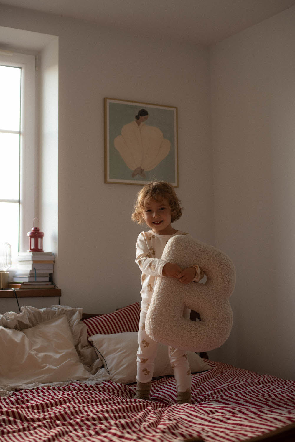 poduszka literka baranek B od Bettys Home którą trzyma w rączkach mały chłopiec stojący na łóżku