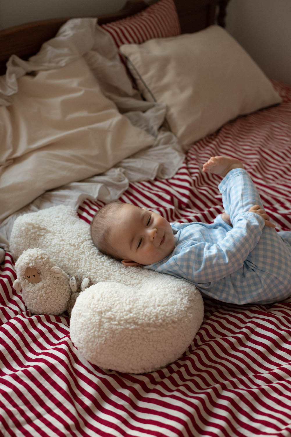 poduszka literka baranek J od Bettys Home na której opiera swoją główkę małe dziecko leżące na łóżku 