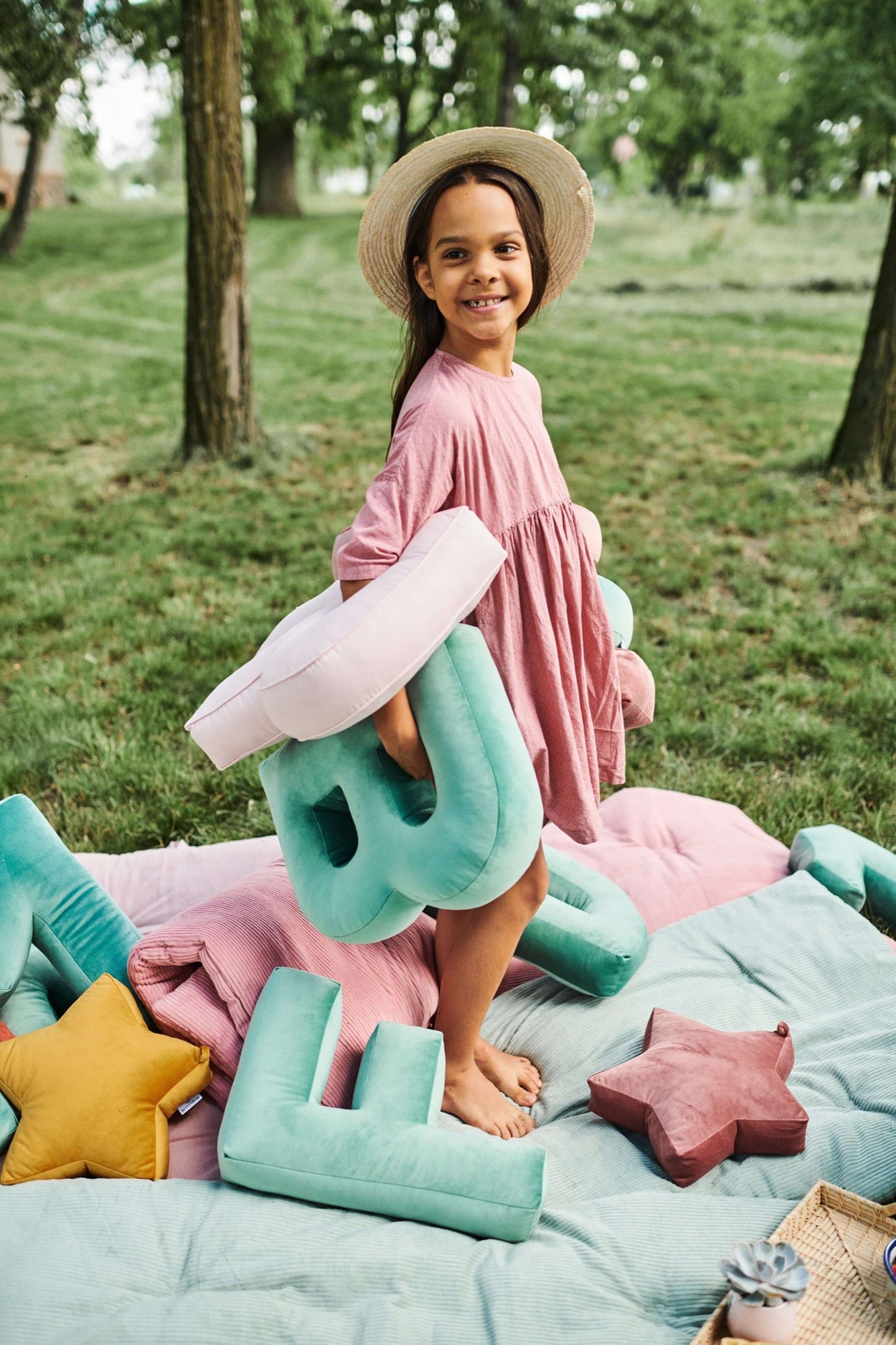 Dziewczynka w ogrodzie w trakcie pikniku trzyma w poduszki literki welurowe od Bettys Home