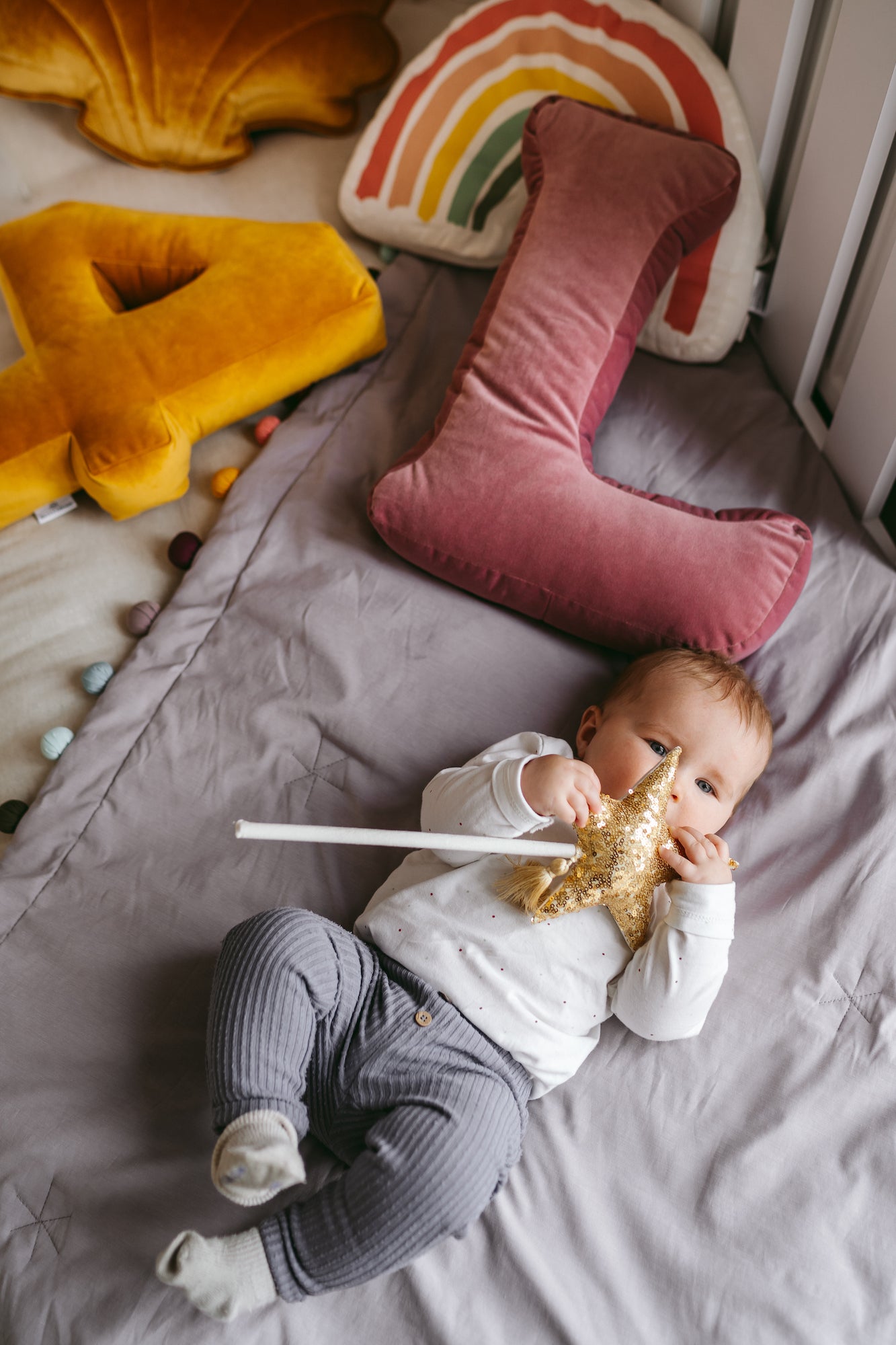 dziecko leżące na łóżeczku w którym są poduszka literka welurowa L oraz poduszka cyferka welurowa 4 od Bettys Home