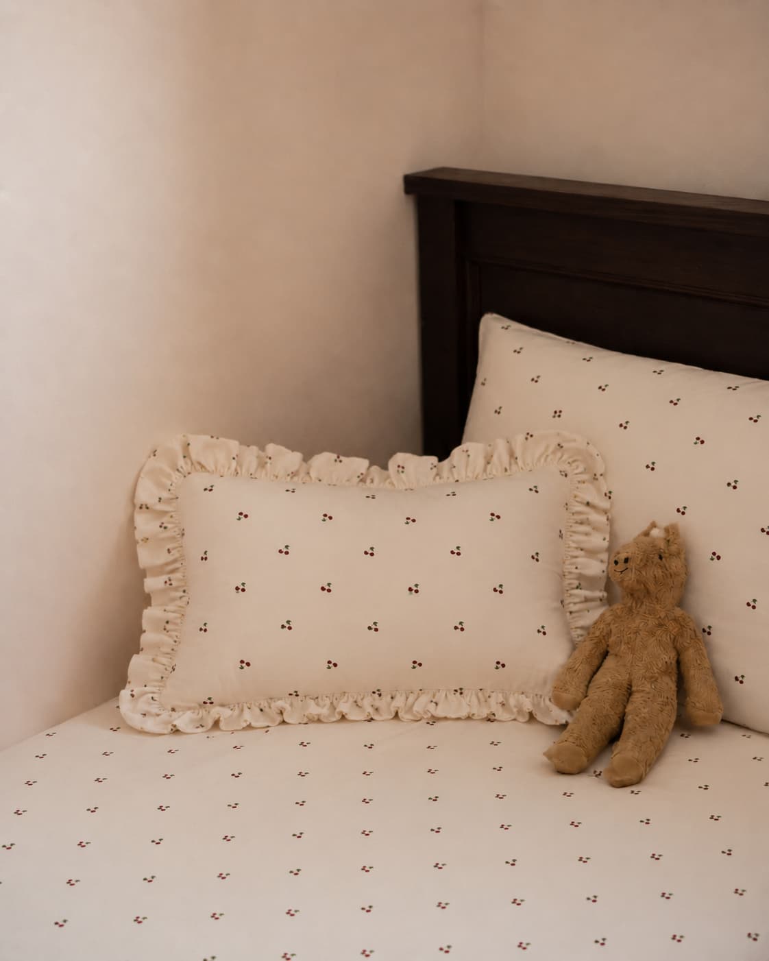 bawełniana poduszka w wiśnie z falbanką od Bettys Home na łóżku obok przytulanki