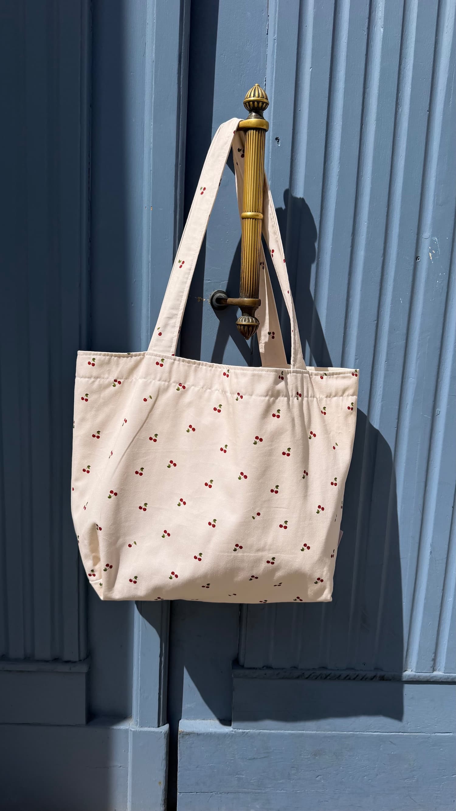 Bawełniana torba Szoperka z nadrukiem wiśni od Bettys Home. Torba tote bag Bettys home wisząca na niebieskich drzwiach