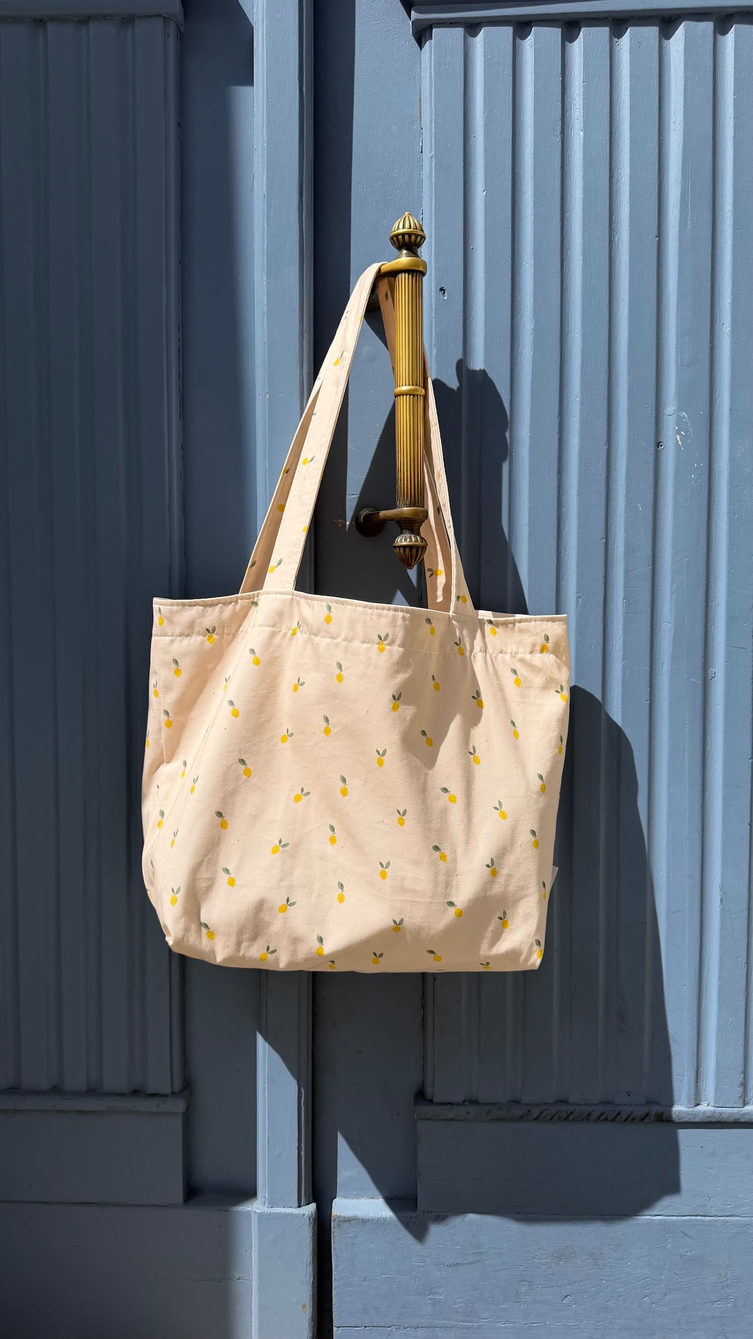 Bawełniana torba Szoperka z nadrukiem cytryn od Bettys Home. Torba tote bag wisząca na niebieskich drzwiach