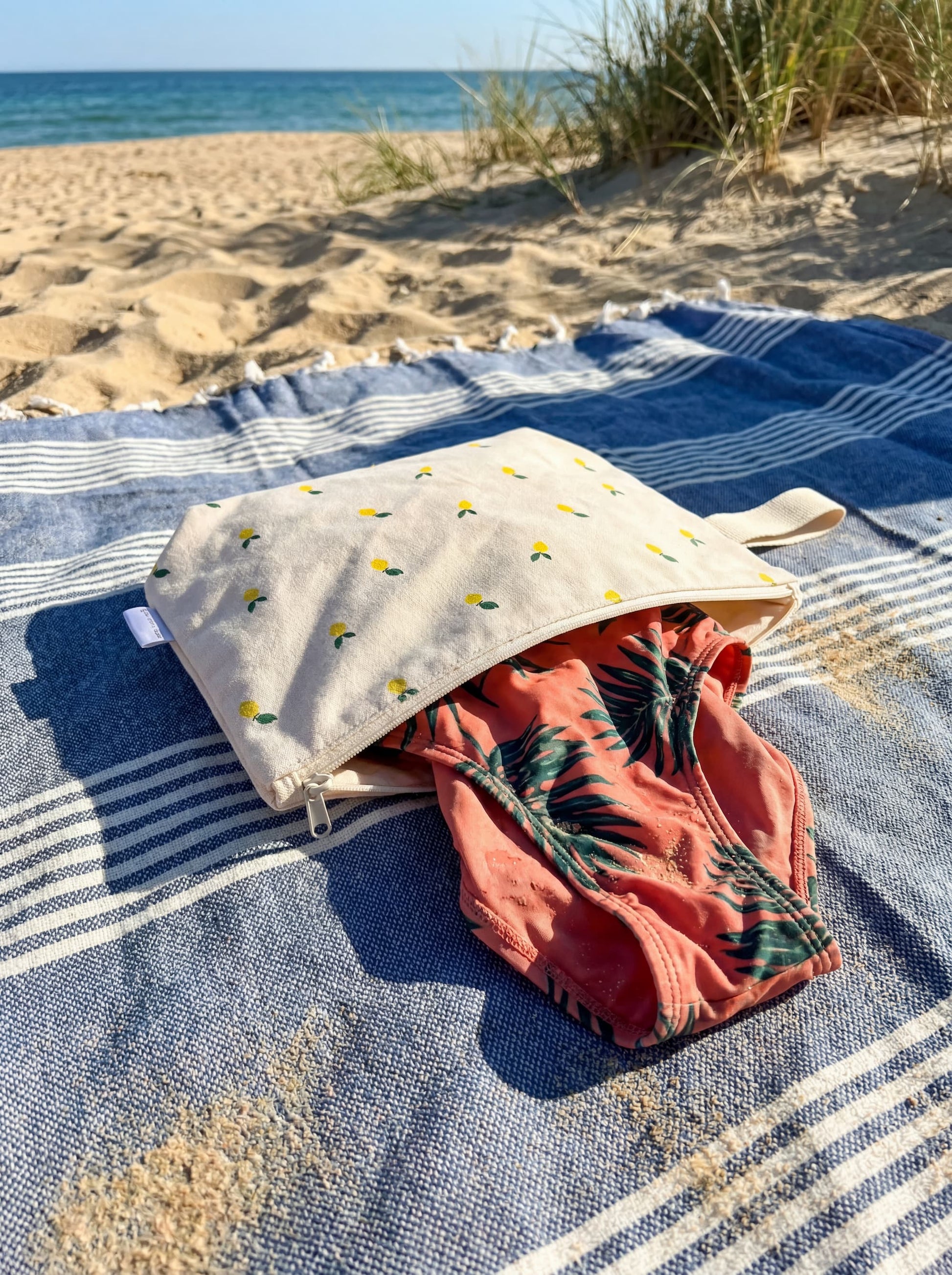 wodoodporna kosmetyczka w cytrynki od Bettys home leży na plaży z mokrym strojem