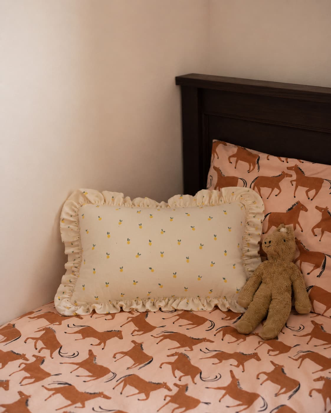 bawełniana poduszka w cytryny z falbanką od Bettys Home na łóżku obok przytulanki