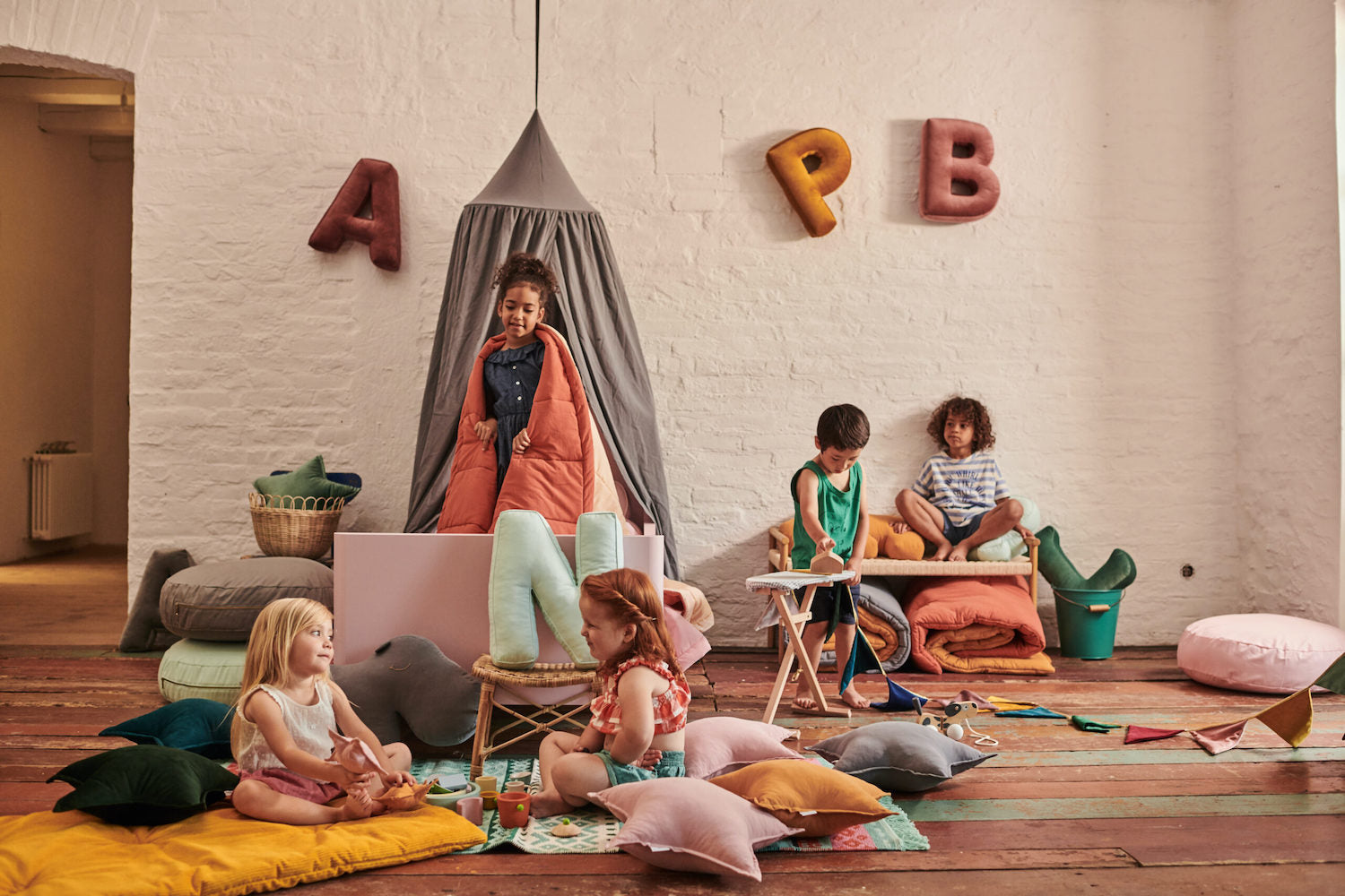 dziewczynki siedzące na podłodze obok poduszek w kształcie gwiazdki a na ścianie są powieszone poduszki w kształcie liter