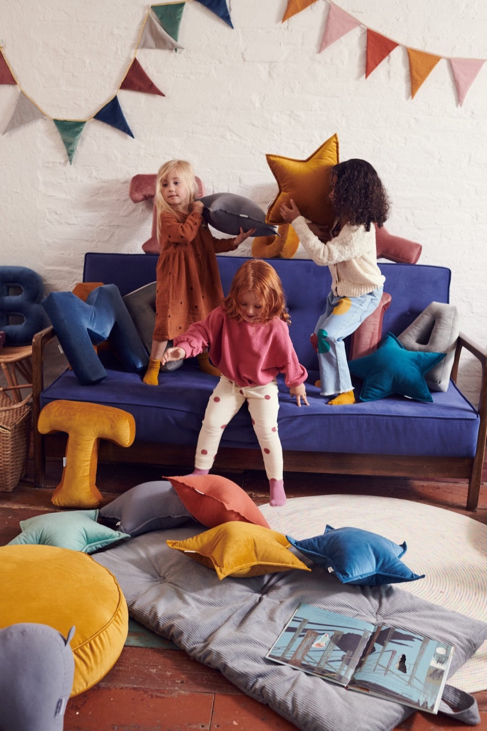 dzieci skaczące na kanapie trzymają w rękach poduszki gwiazdki od bettys home. Na podłodze leży pufa welurowa od bettys home