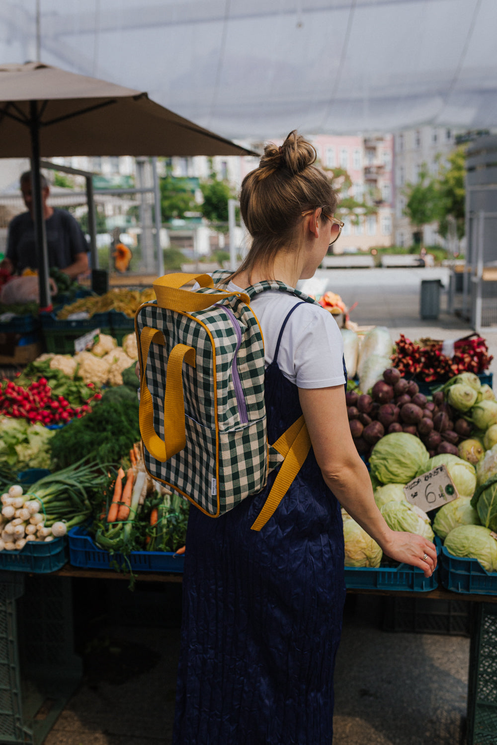 kobieta na zakupach przy stoisku z owocami nosi na plecach zielony plecak w kratkę od Bettys Home, plecak do szkoły damski 