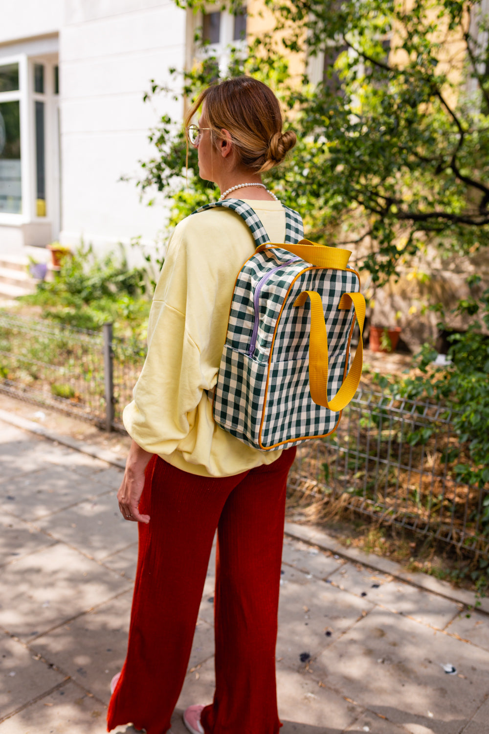kobieta w żółtej bluzie z zielonym plecakiem w kratkę od Bettys Home w drodze przez miasto, plecak do szkoły dla dziewczynek