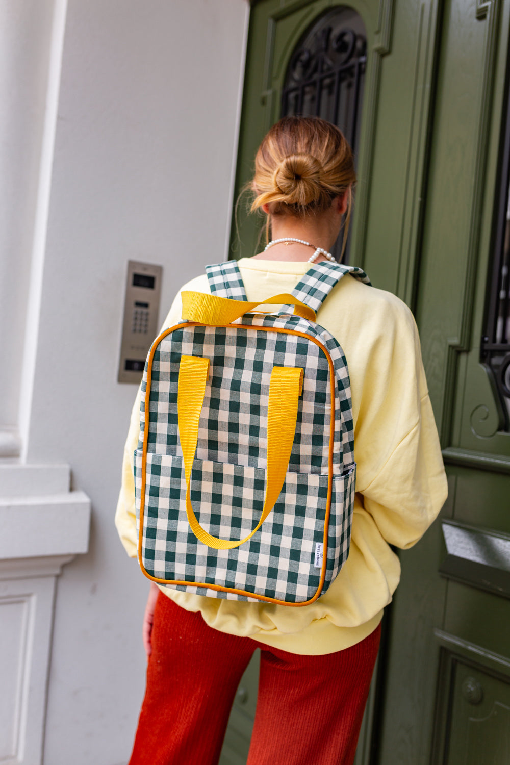 kobieta przed drzwiami domu z plecakiem w kratkę zielonym od Bettys Home, elegancki plecak na laptopa damski