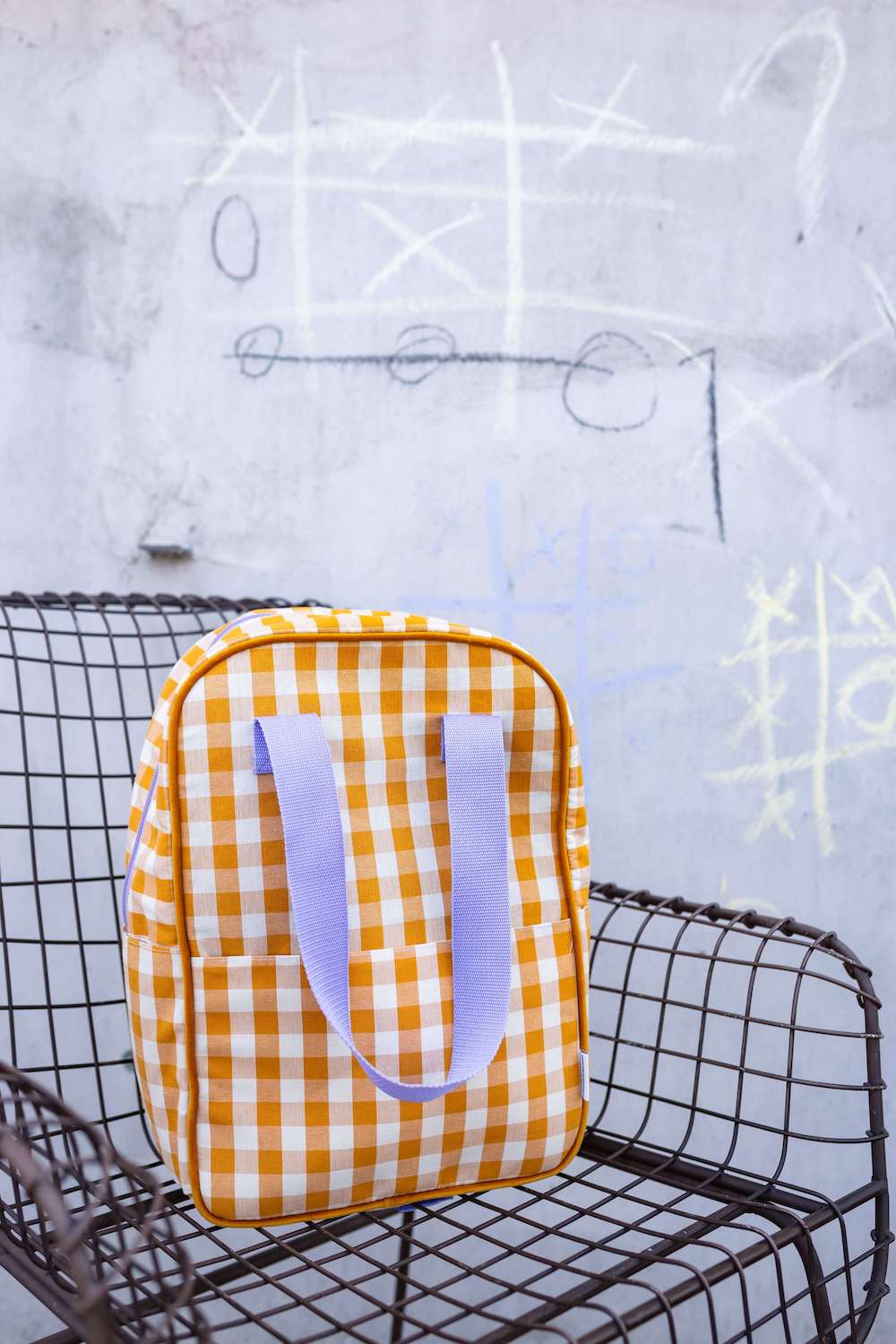 żółty plecak w kratkę z fioletowymi paskami od Bettys Home stojący na krześle na dworze. plecak do szkoły dla nastolatków