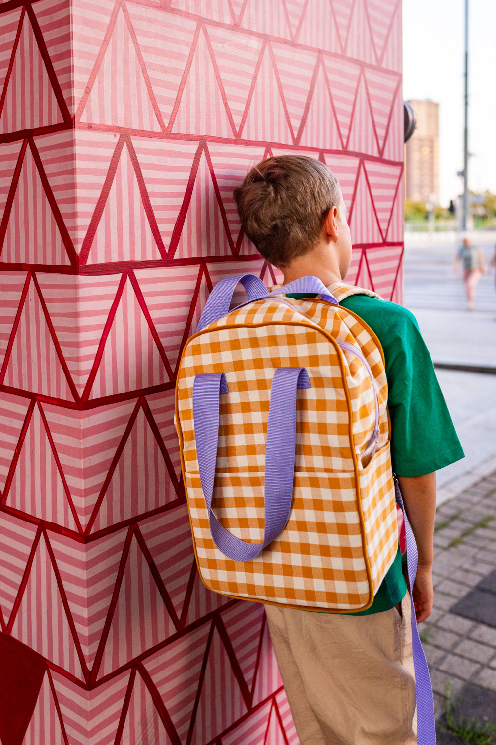 chłopiec oparty o kolorową ścianę stoi z plecakiem w kratkę w kolorze żółtym od Bettys Home plecak młodzieżowy
