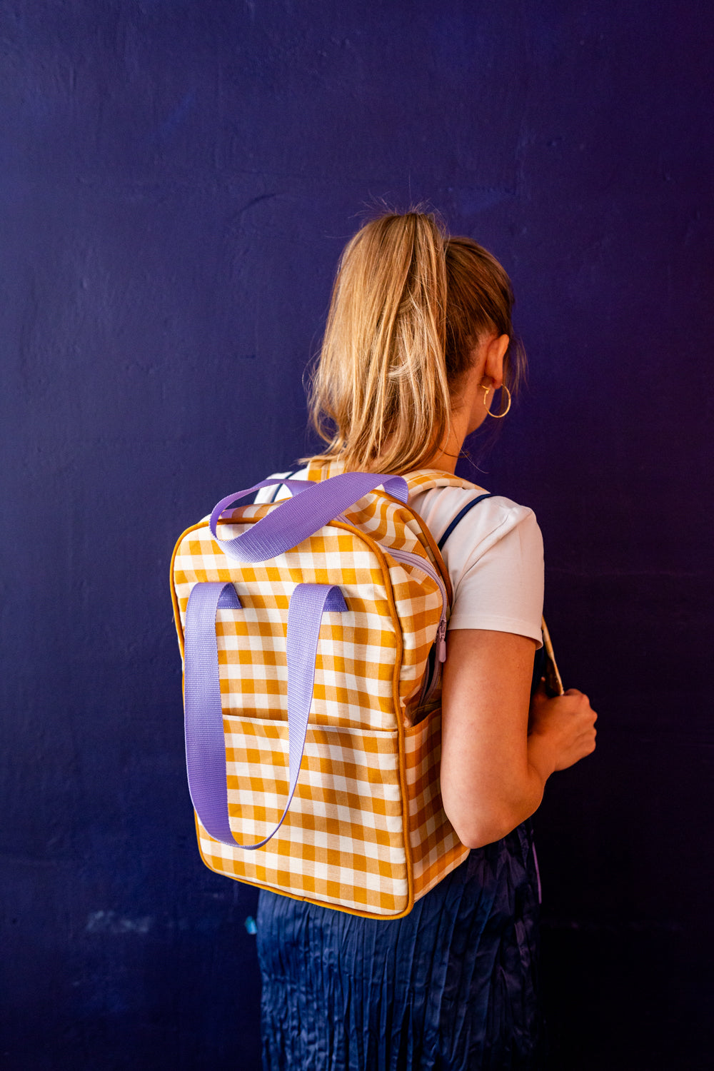 młoda kobieta na tle niebieskiej ściany stoi z plecakiem żółtym w kratkę od bettys home plecak do szkoły średniej