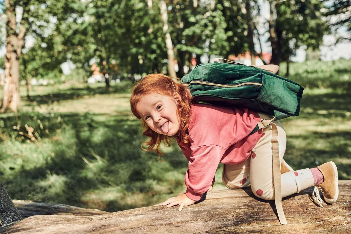 dziewczynka chodzi po drzewie z dużym plecakiem welurowym od Bettys Home zielonym, plecak do szkoły dla dziewczynki
