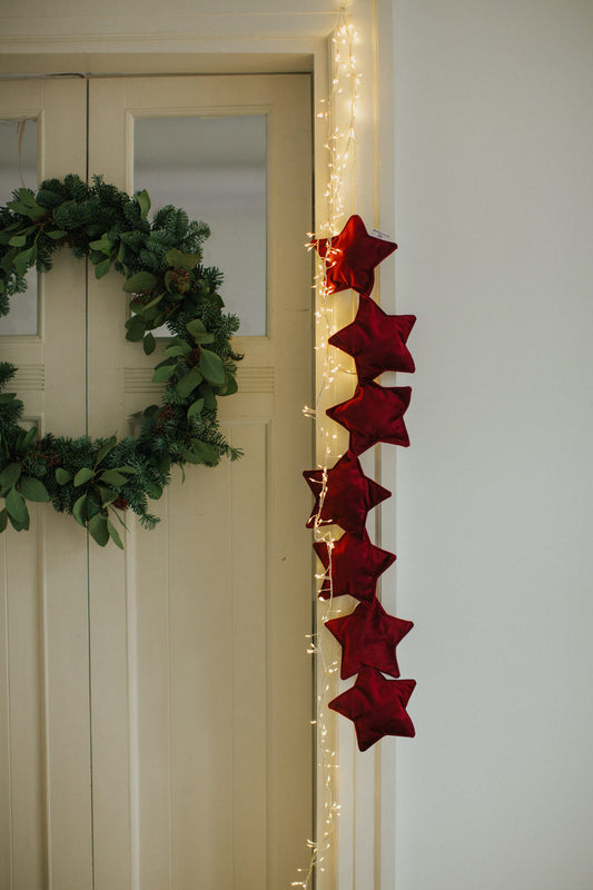 Girlanda z gwiazdek welurowych w kolorze czerwonym wino od Bettys Home wisząca na futrynie od drzwi jako świąteczna dekoracja