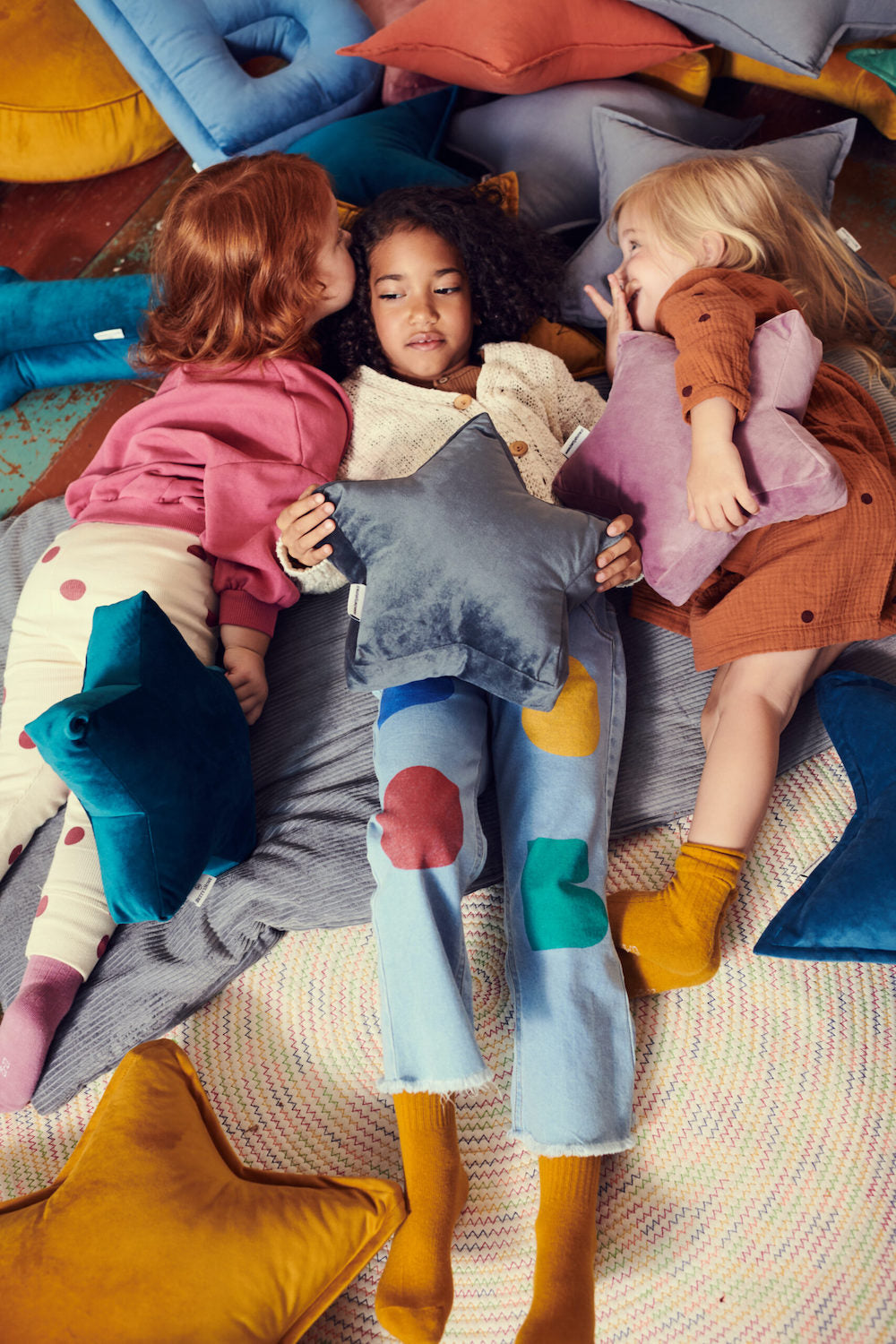dziewczynki leżące na podłodze pośród różnych poduszek welurowych od bettys home trzymają w ręce poduszki gwiazdki welurowe