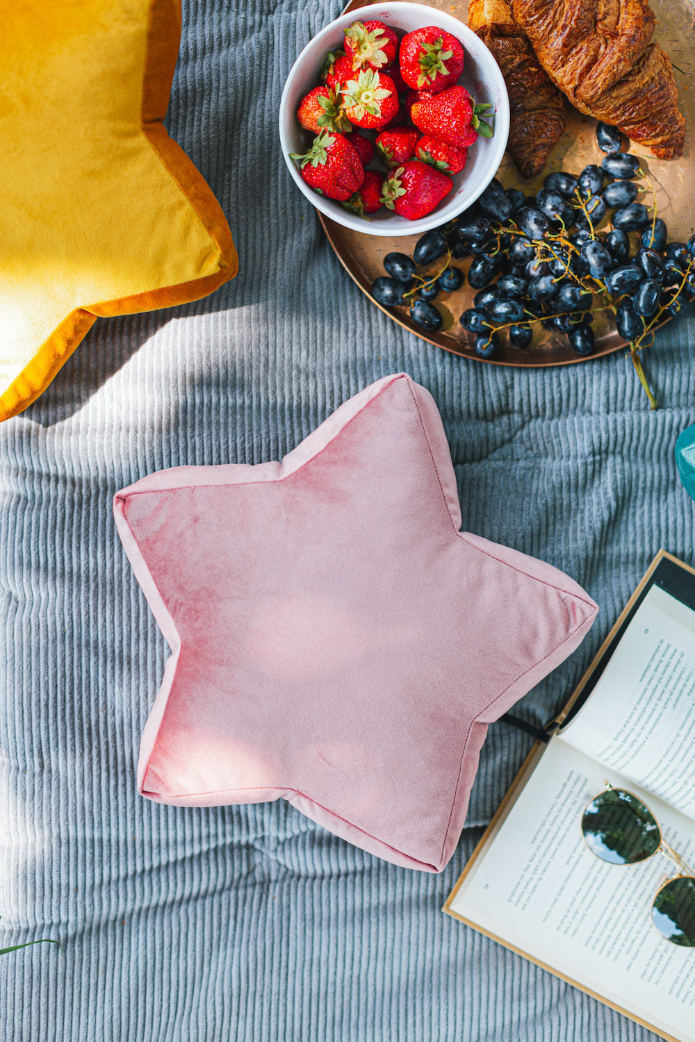 mała poduszka gwiazdka welurowa w kolorze różowym od bettys home leży obok książki i miski z truskawkami 