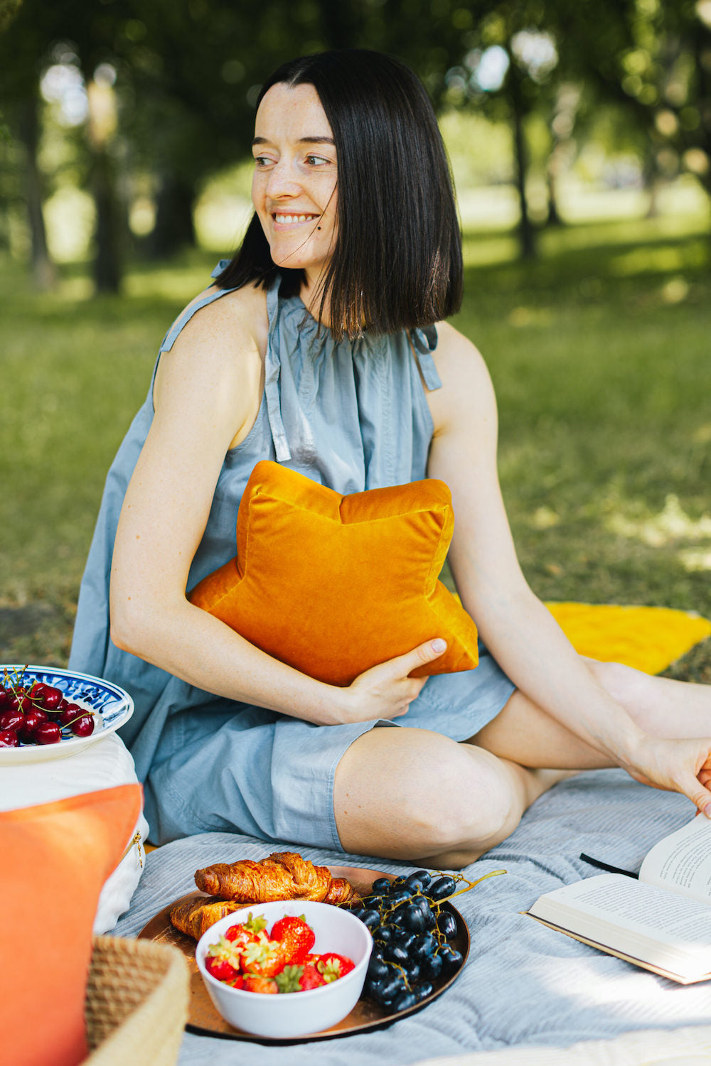 kobieta w parku w trakcie pikniku trzyma w rękach małą poduszkę gwiazdkę welurową od bettys home. pomysł na urodziny