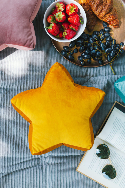 mała poduszka gwiazdka żółta od Bettys Home na kocu w trakcie pikniku obok książka, truskawki i rogalik