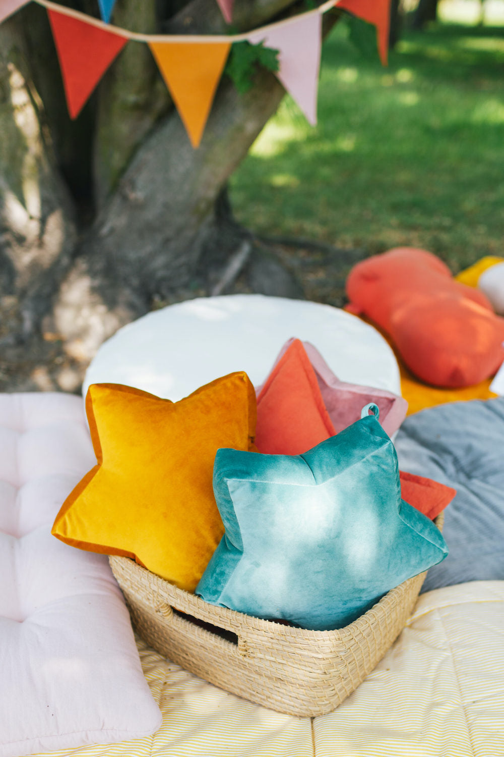 wiklinowy koszyk na kocu w parku w którym są małe poduszki gwiazdki welurowe od Bettys Home. wiszące ozdoby do pokoju 