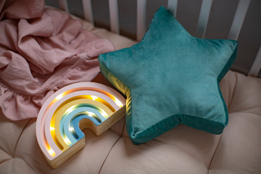 Mała poduszka gwiazdka welurowa miętowa od Bettys Home leżące w dziecięcym łóżeczku rok lampki w kształcie tęczy.