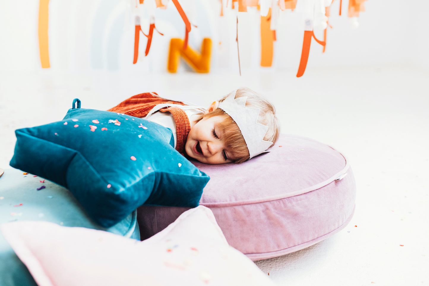 mała dziewczynka leżącą na dużej pufie welurowej w kolorze różowym od bettys home obok małej poduszki gwiazdki zawieszki