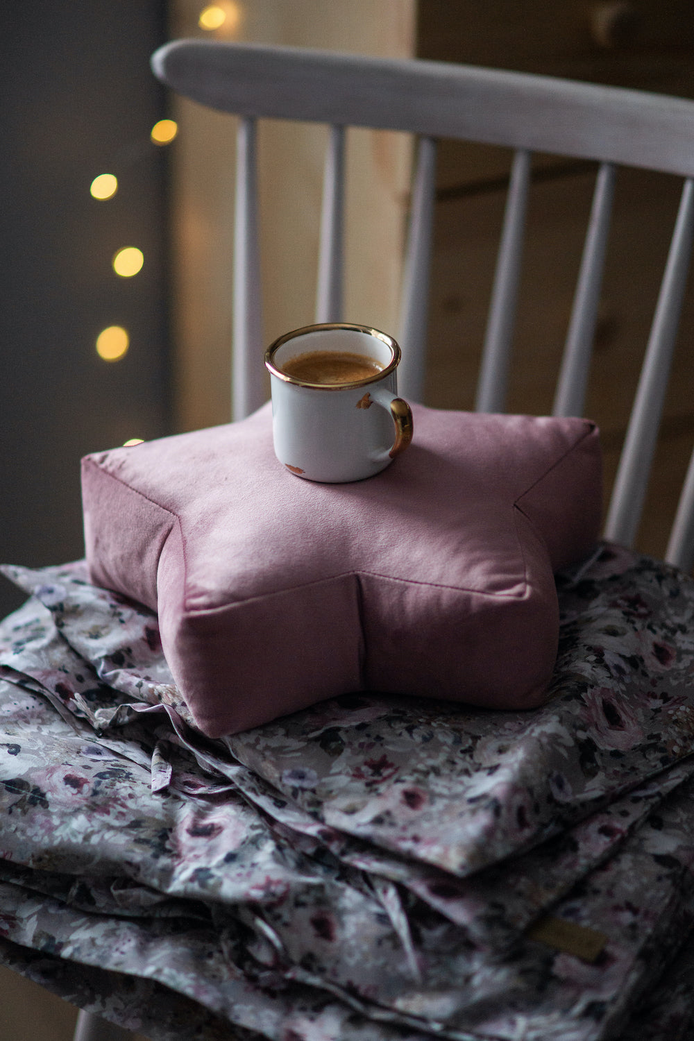 mała poduszka gwiazdka welurowa w kolorze różowym na której stoi kubek z kawą. Gwiazdka leży na krześle. dekoracje pokoju