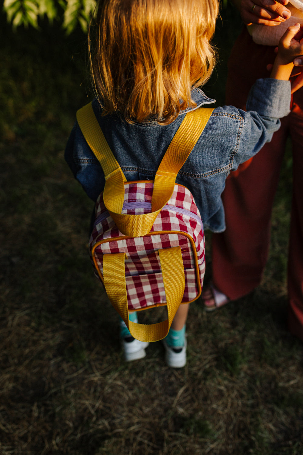 mały chłopiec w parku z małym czerwonym plecakiem w kratkę od Bettys Home, plecak do szkoły dla dziewczynek 
