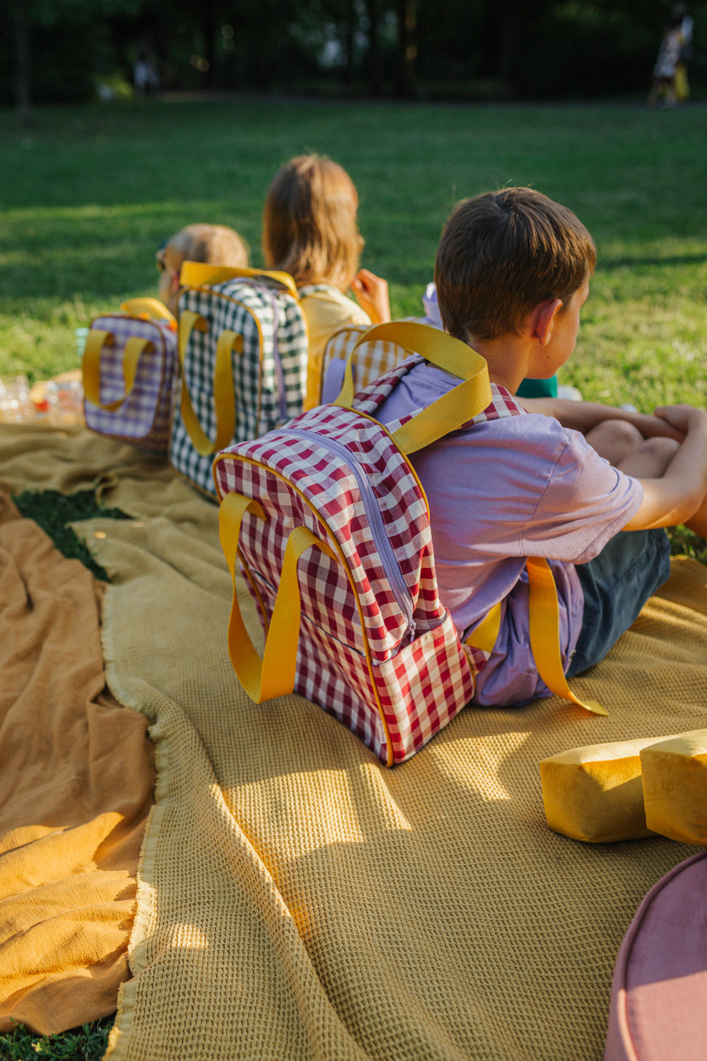 dzieci siedzące w parku na żółtym kocu, każdy z nich ma plecak w kratkę od Bettys Home, plecak do szkoły dla nastolatków 