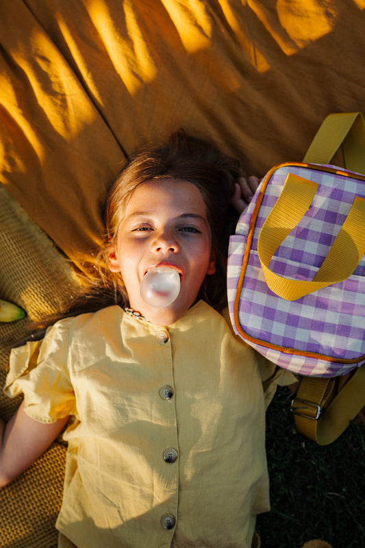 dziewczynka leżąca na kocu a obok niej mały plecak w żółtą kratkę od Bettys Home, plecak do szkoły dla dziewczynek 