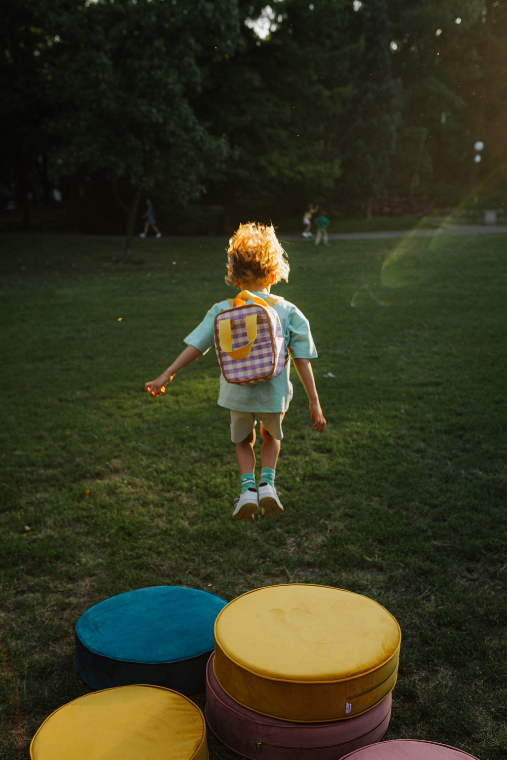 Mały chłopiec z plecakiem fioletowym w kratkę od Bettys Home skacze z dużej pufy welurowej, plecak do szkoły dla chłopca 