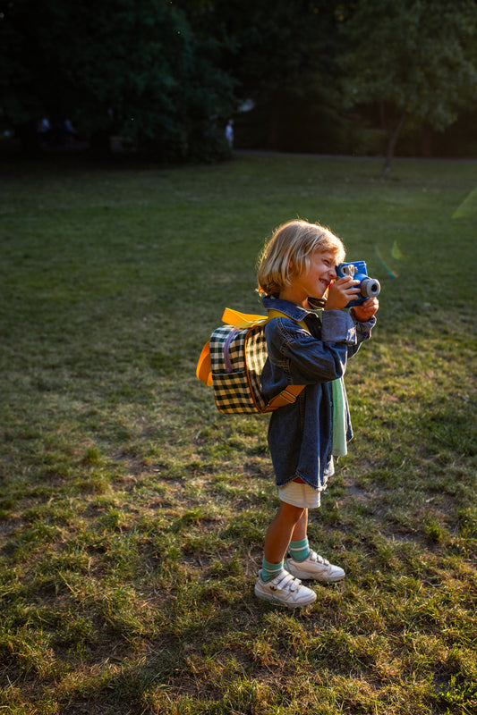mały chłopiec w parku z małym zielonym plecakiem w kratkę od Bettys Home robiący zdjęcia, plecak do przedszkola