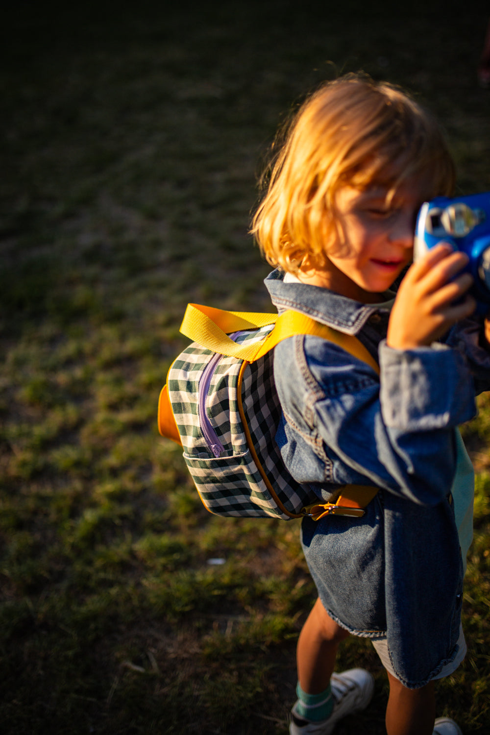 mały chłopiec w parku z małym zielonym plecakiem w kratkę od Bettys Home robiący zdjęcia, plecak dla dziecka