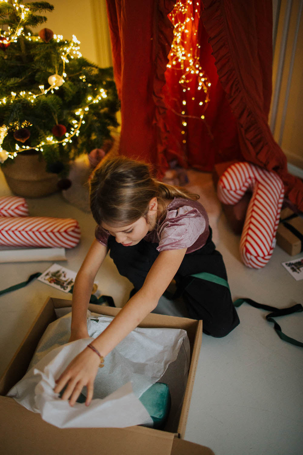 świąteczną poduszką laską w biało czerwone paski od Bettys Home leżące pod choinką otwieranie prezentów
