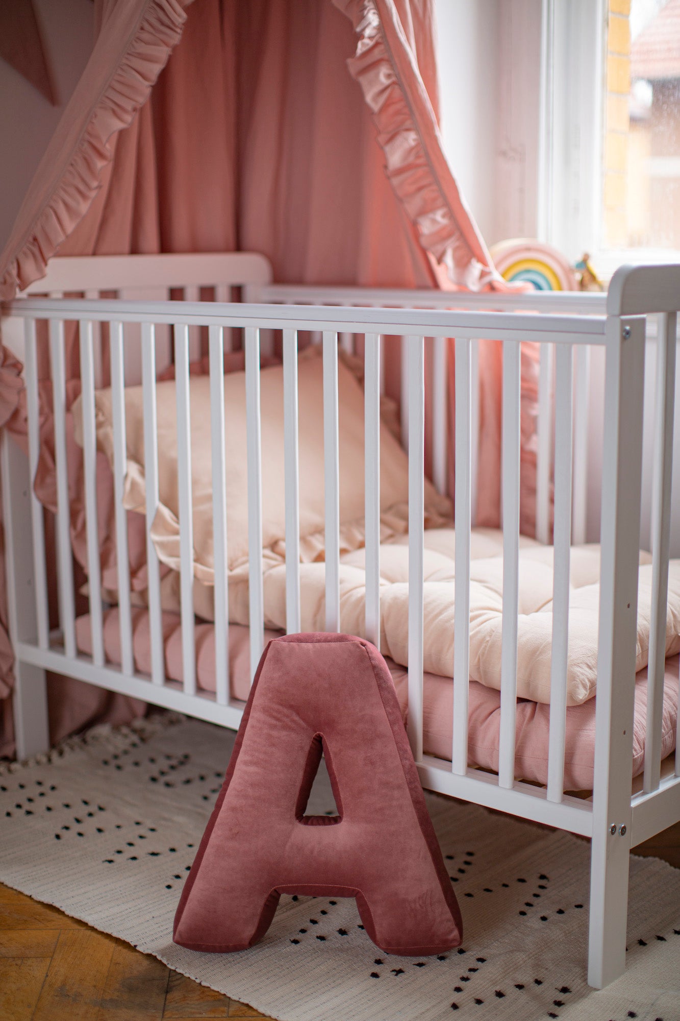 Poduszka literka welurowa A w kolorze różowym przed dziecięcym łóżeczkiem od bettys home