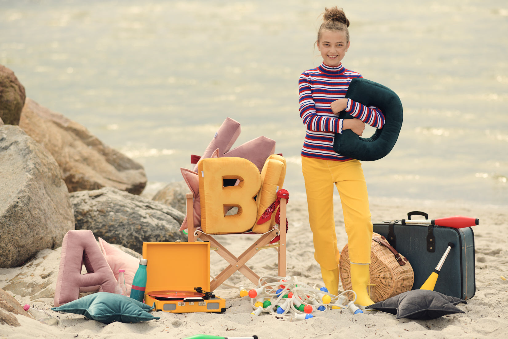urocza dziewczynka stojąca na plaży i trzymająca welurową poduszkę literkę D od Bettys Home