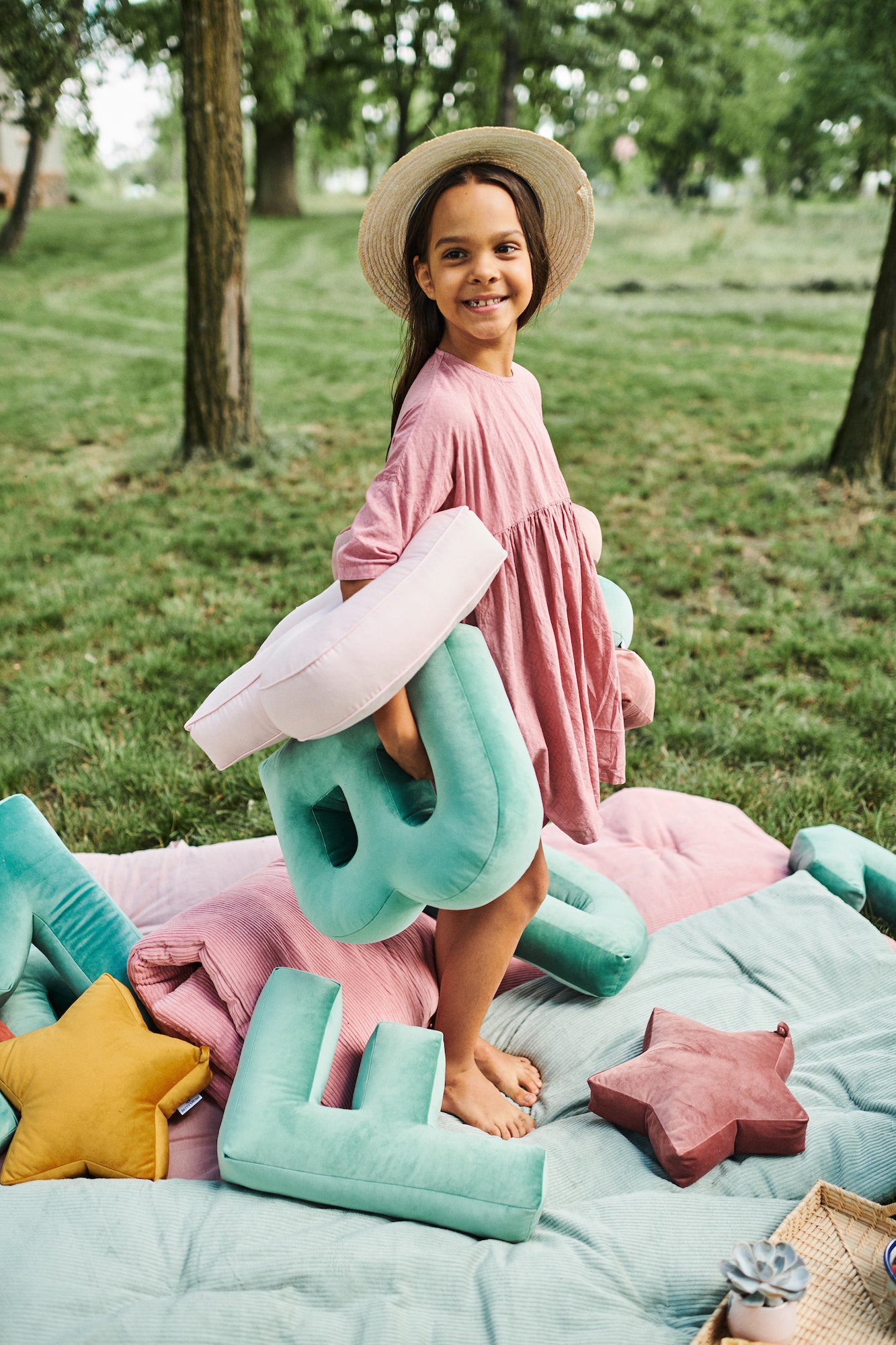 dziewczynka w różowej sukience w parku na trawie trzyma poduszki literki welurowe od Bettys Home