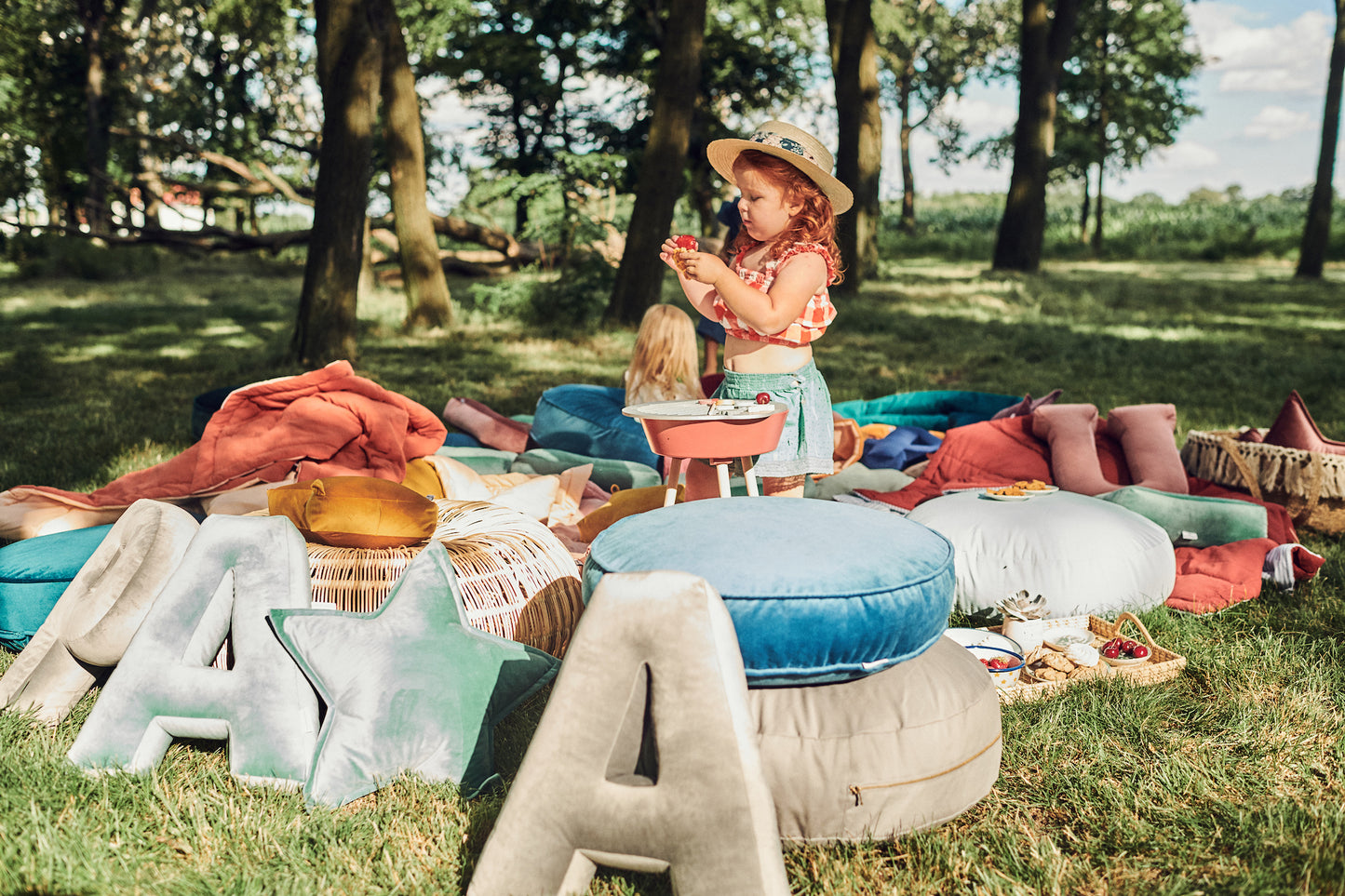piknik dziecięcy w parku z poduszkami literkami welurowymi od Bettys Home. Obok dziecka są duże pufy welurowe