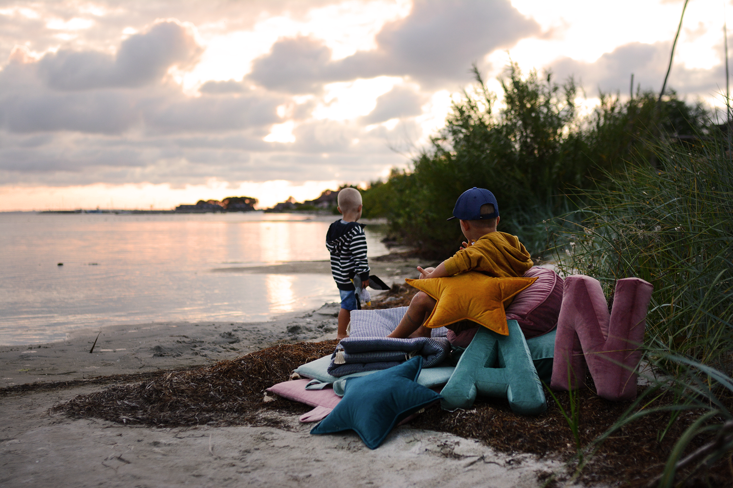 dwóch braci na plaży w trakcie zachodu słońca obok poduszek literek welurowych A miętowa i N różowa od Bettys Home