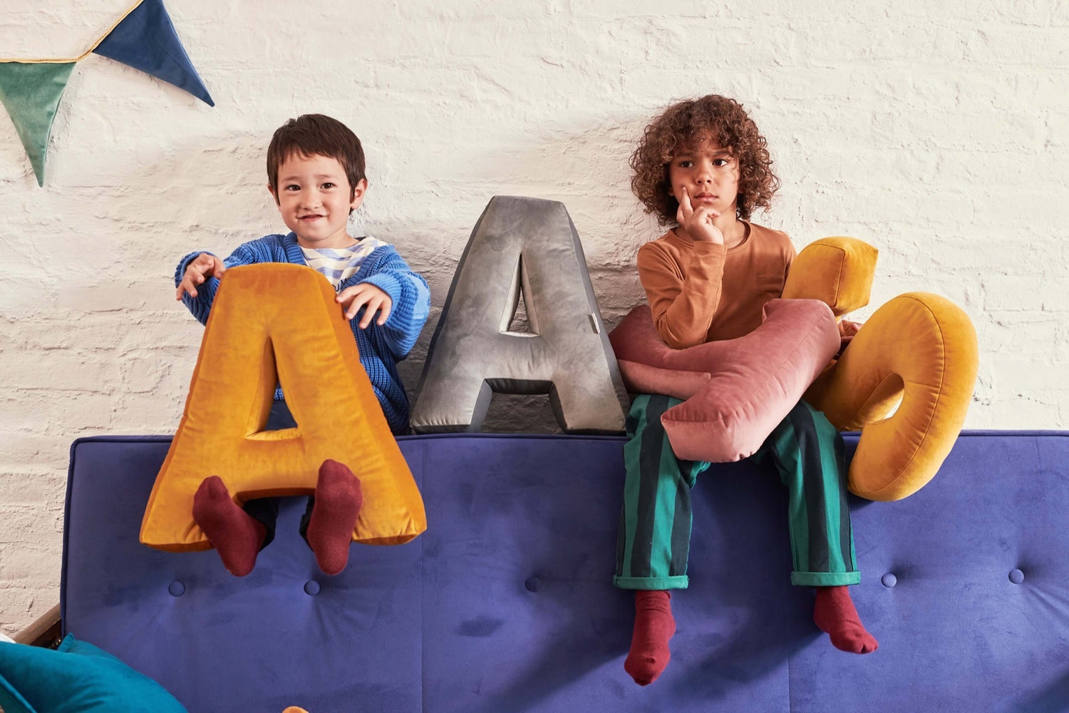 chłopcy siedzący na kanapie z poduszkami literkami welurowymi A i S w kolorze żółtym od Bettys Home