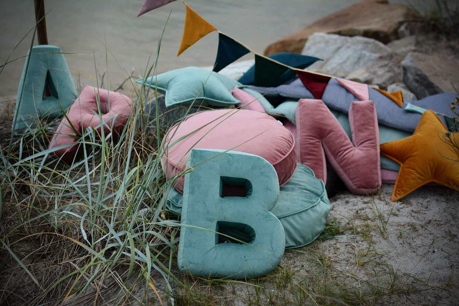Poduszki literki i pufy welurowe od Bettys Homer leżące na plaży 