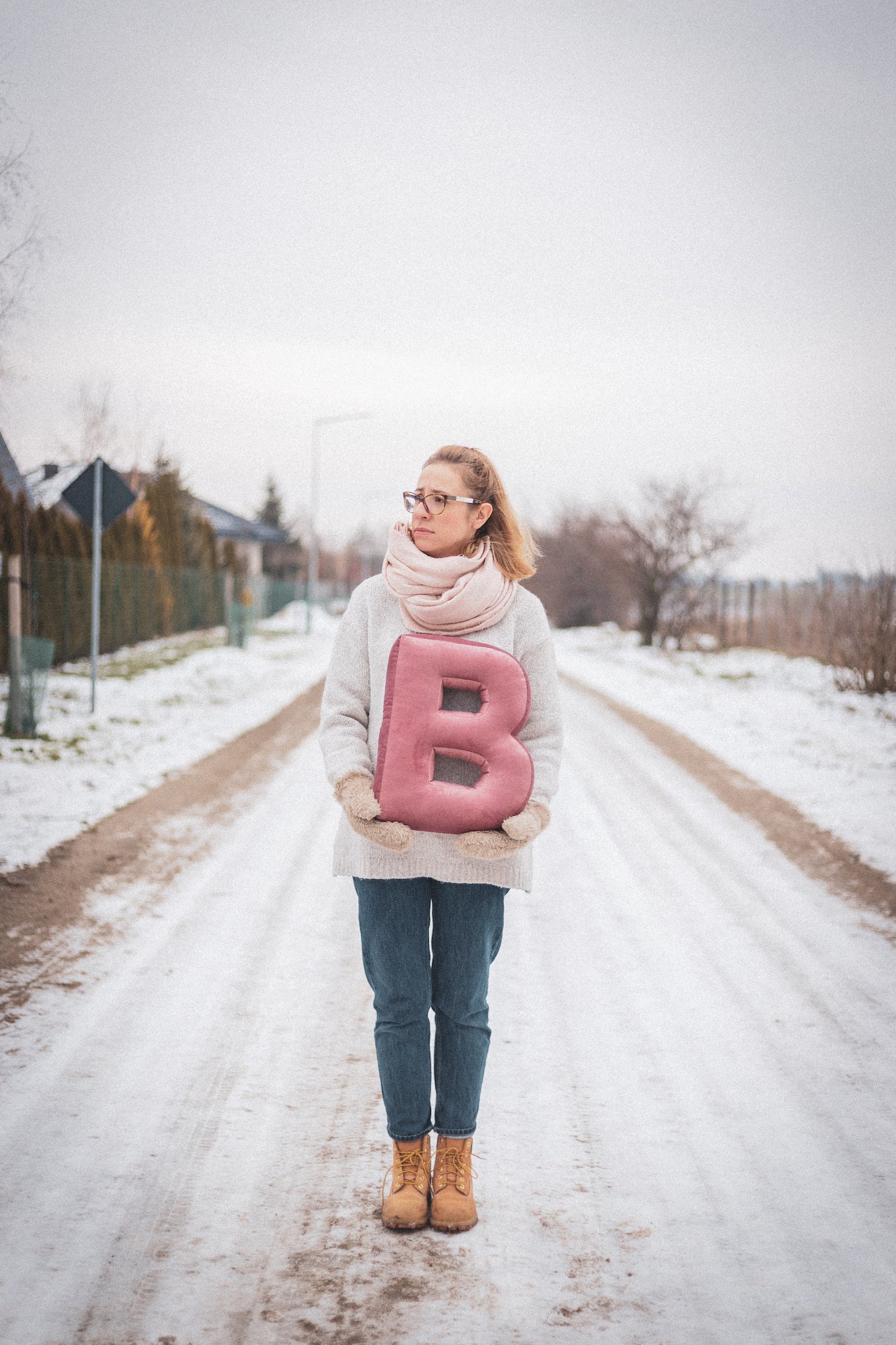 kobieta stojąca w zimie na dworze trzymająca w rękach poduszkę literkę welurową B w kolorze różowym od bettys home