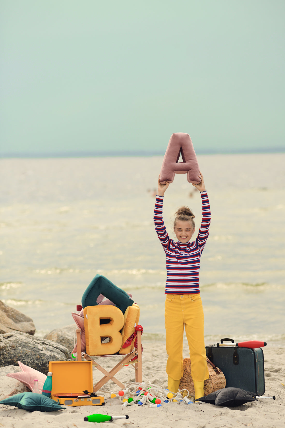 czarująca dziewczynka nad morzem trzymająca poduszkę literkę welurową A w kolorze różowym nad głową