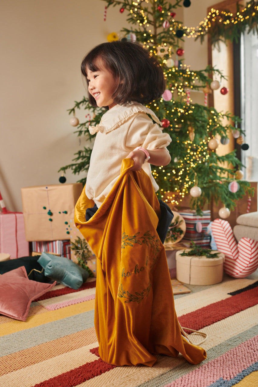 mała dziewczynka która stoi w welurowym żółtym worku na prezenty obok choinki