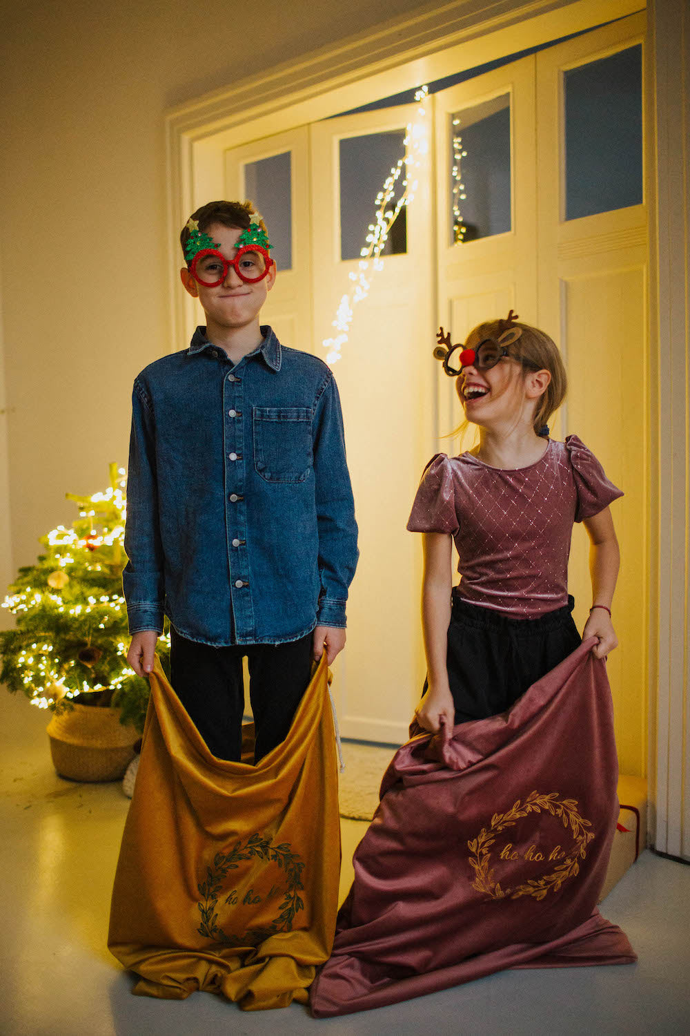 chłopiec i dziewczynka ze świątecznymi okularami trzymają w ręce worki na prezenty welurowe od Bettys Home