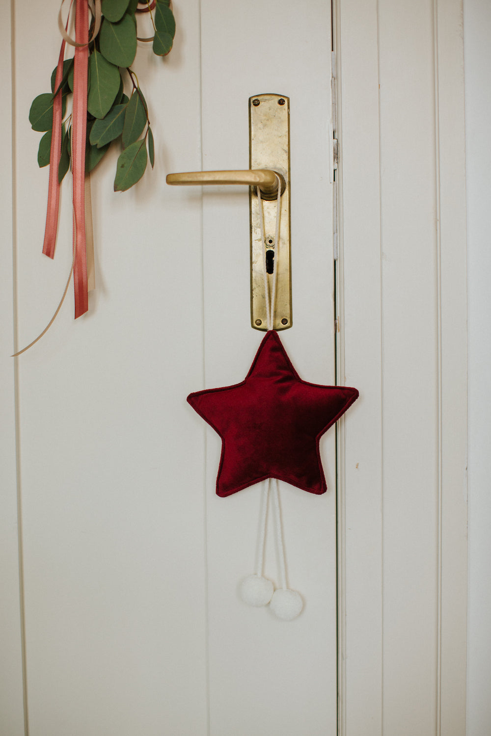 mała zawieszka gwiazdka w kolorze czerwonym z pomponami wisząca na klamce od drzwi 